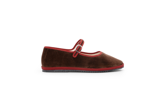 A brown velvet slipper with a Maryjane style closure and a flat sole.