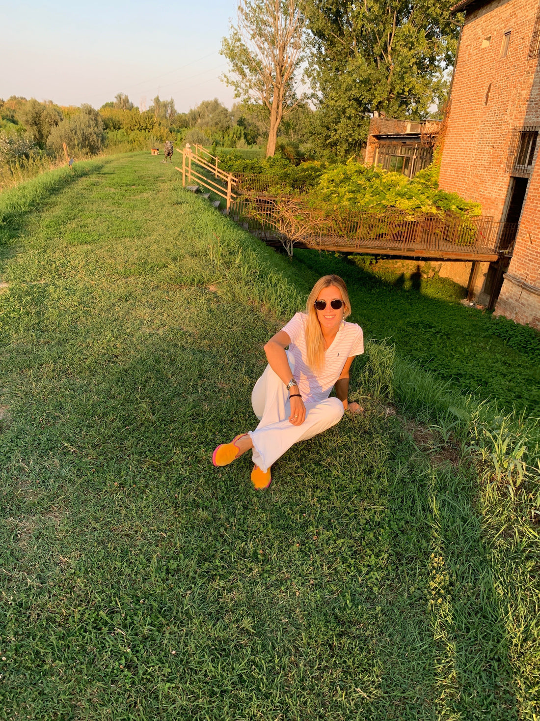 A woman sitting on grassy land in the Parma Countryside during sunset, enjoying the serene nature.