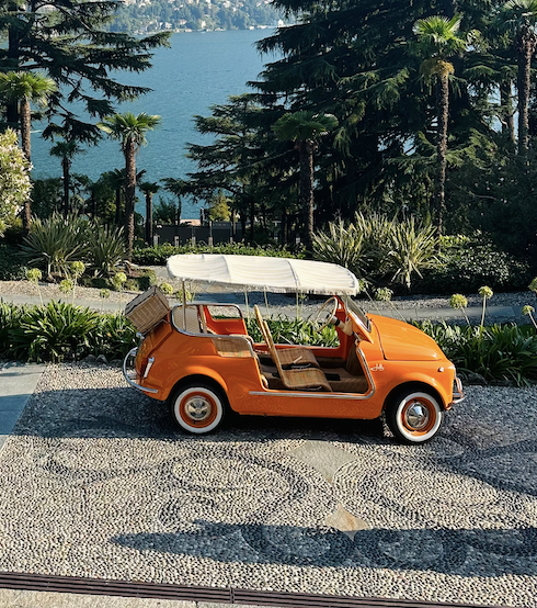 A Taste of Milan & Lake Como with a local, an orange vintage car parked by the lake surrounded by lush greenery.